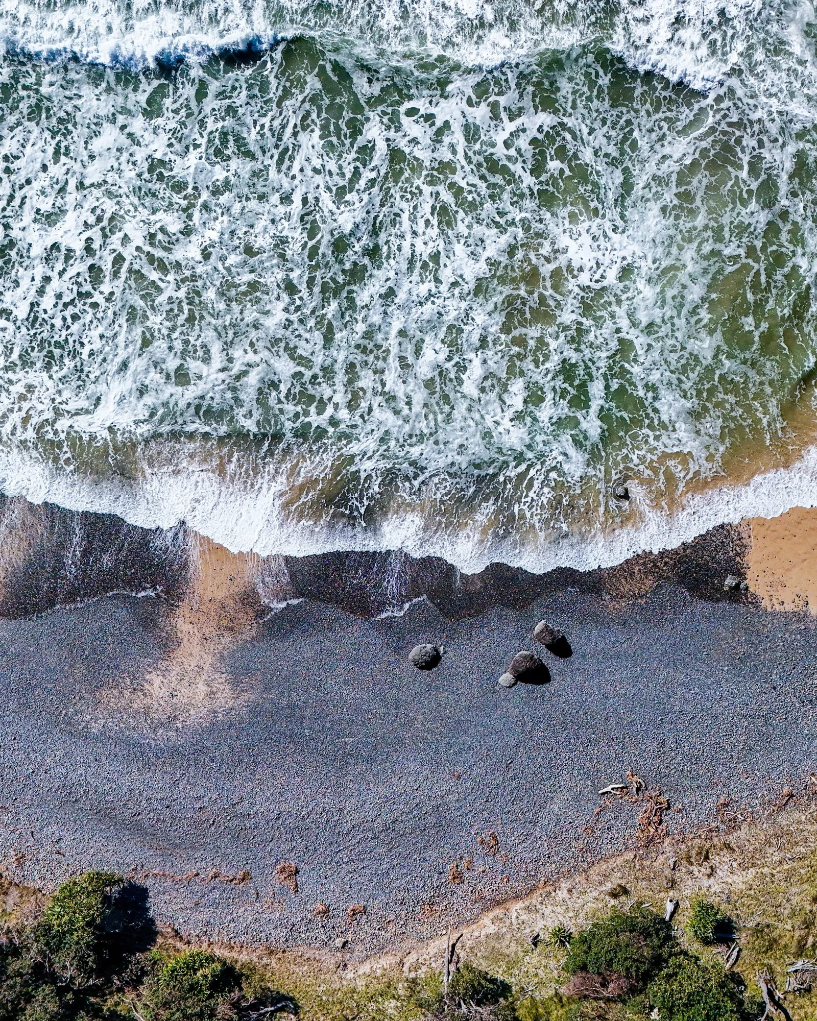 Drone view straight down over surf breaking onto a pebble beach on the Northern Rivers coast, by Kris Cook
