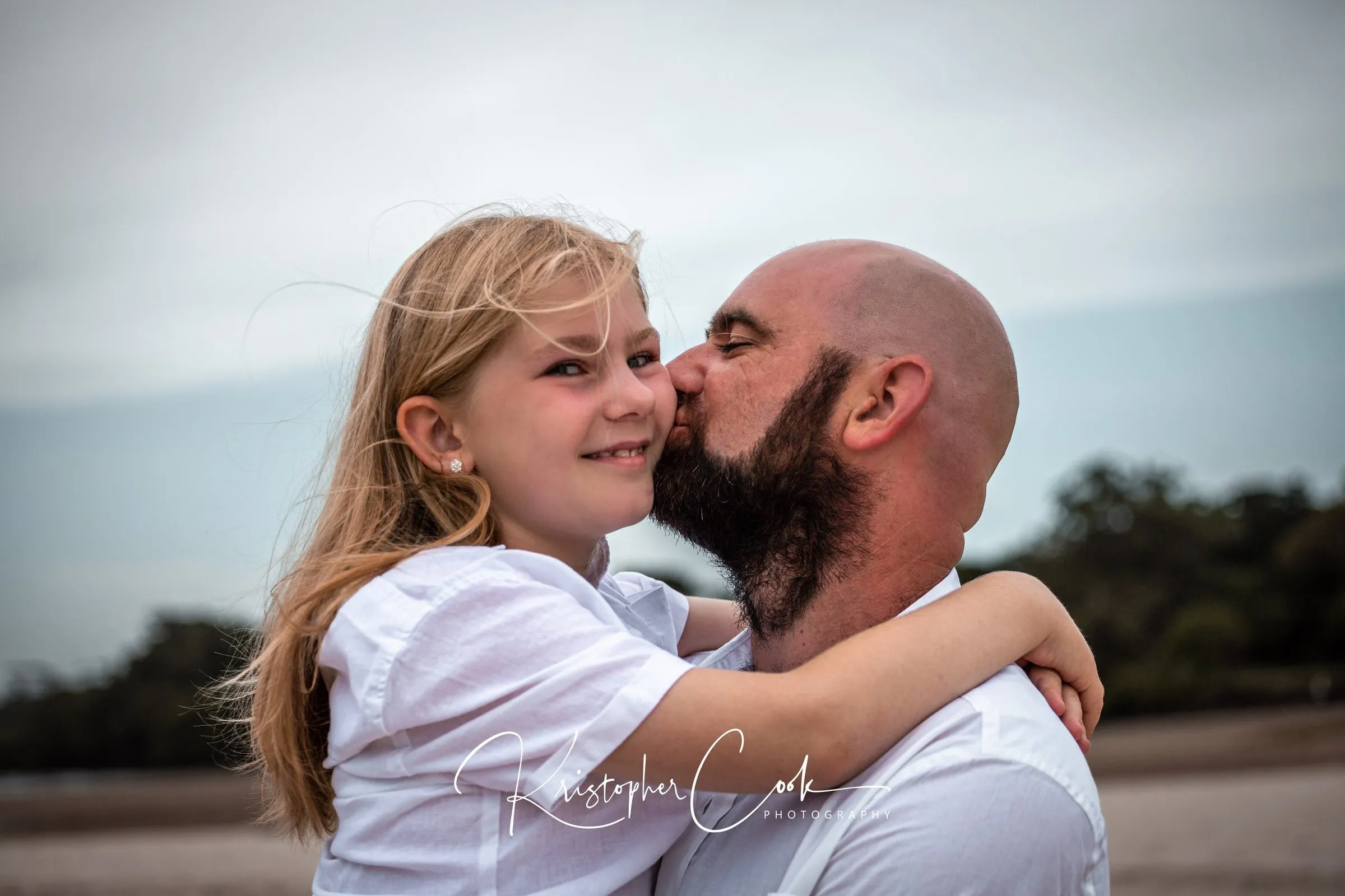 Father and daughter laughing on the beach, photographed by Kris Cook